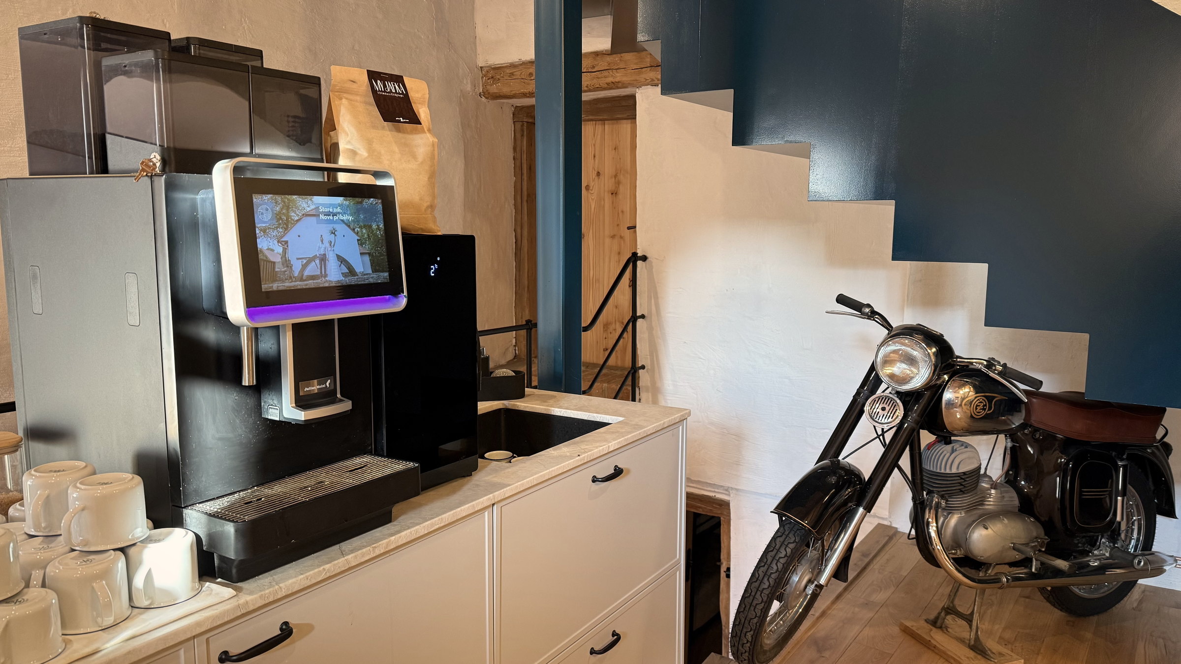 Samoobslužná coffee station v mlýnici Kománkova mlýna, vedle motocykl Jawa a modré schodiště