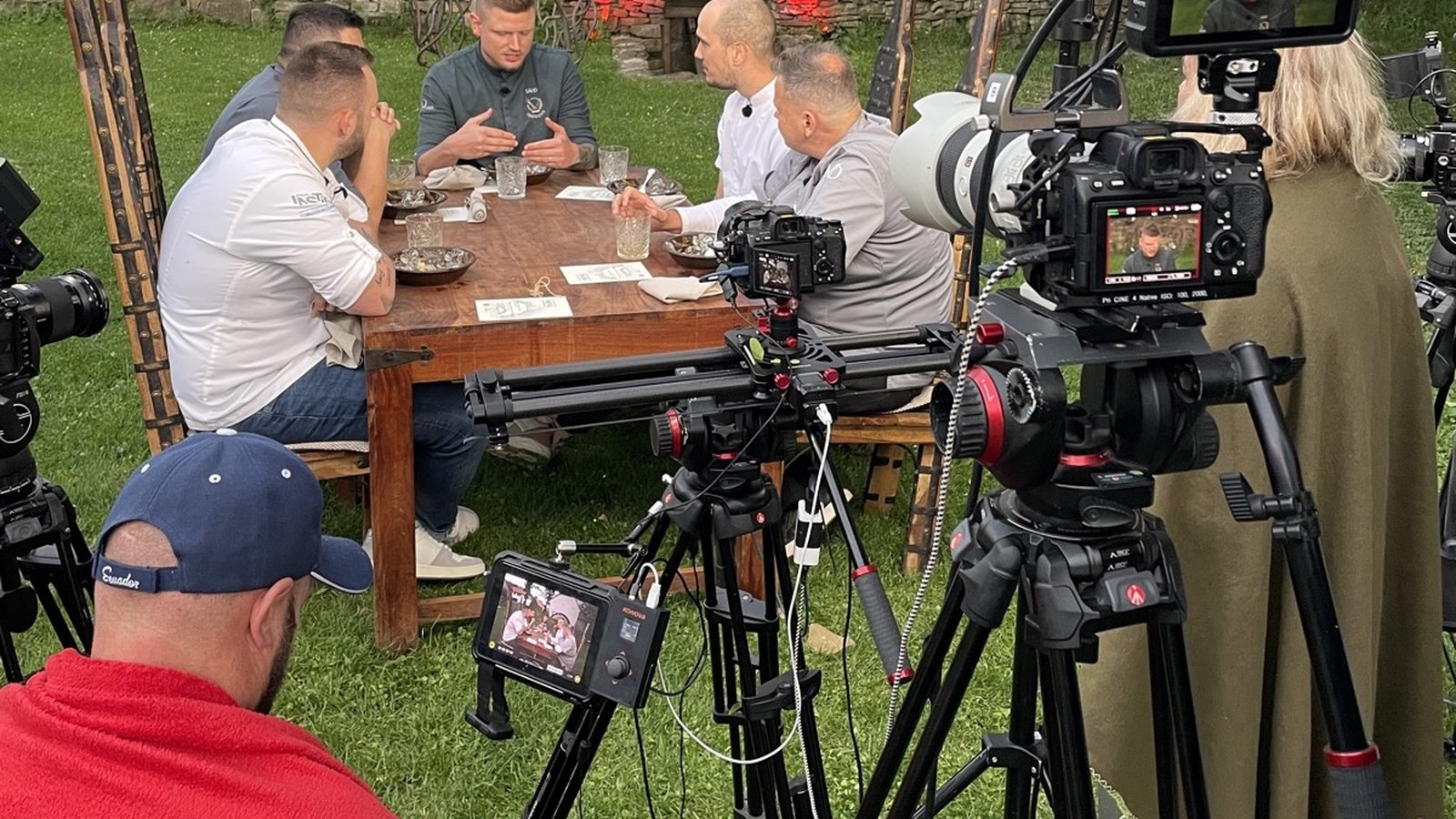 Filmový štáb s kamerami natáčí pět šéfkuchařů u dřevěného stolu na nádvoří Kománkova mlýna