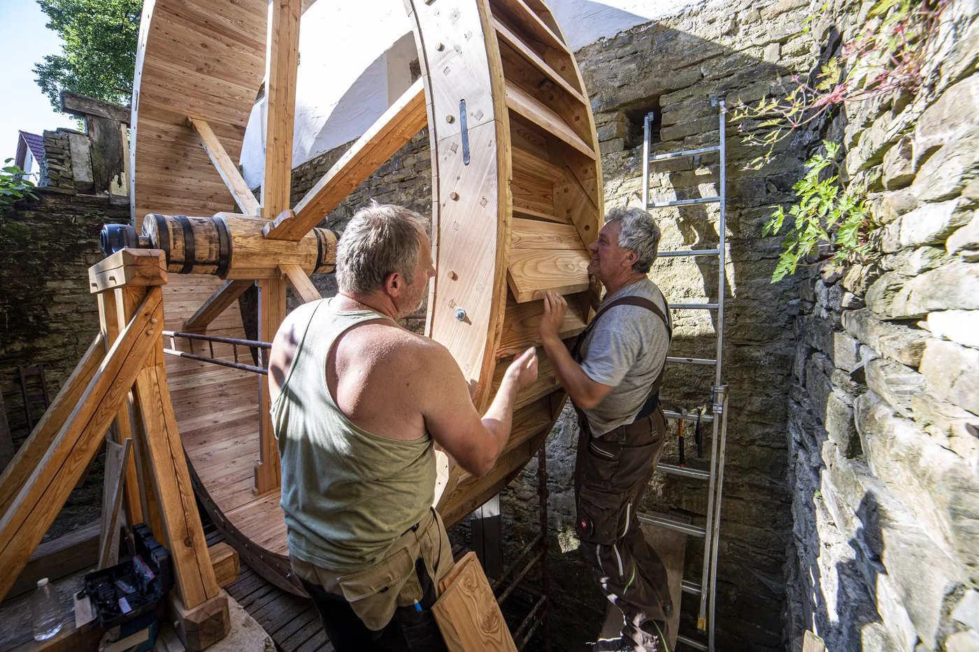 Two millwrights fitting a wooden blade into the assembled mill wheel