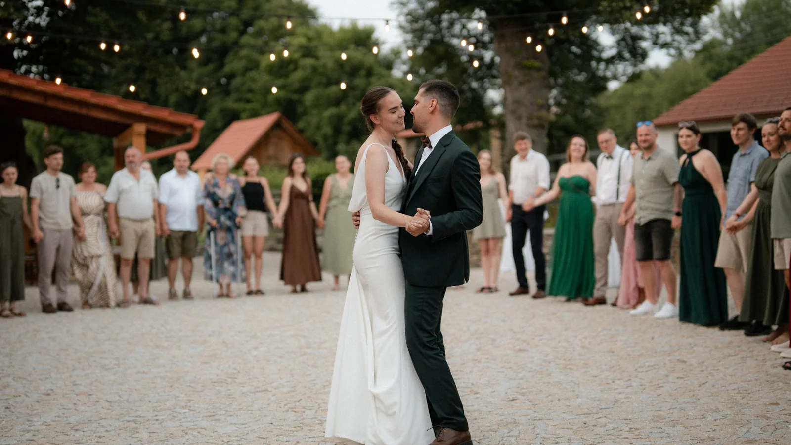 The first dance in the mill courtyard at dusk, guests standing in a ring under string lights
