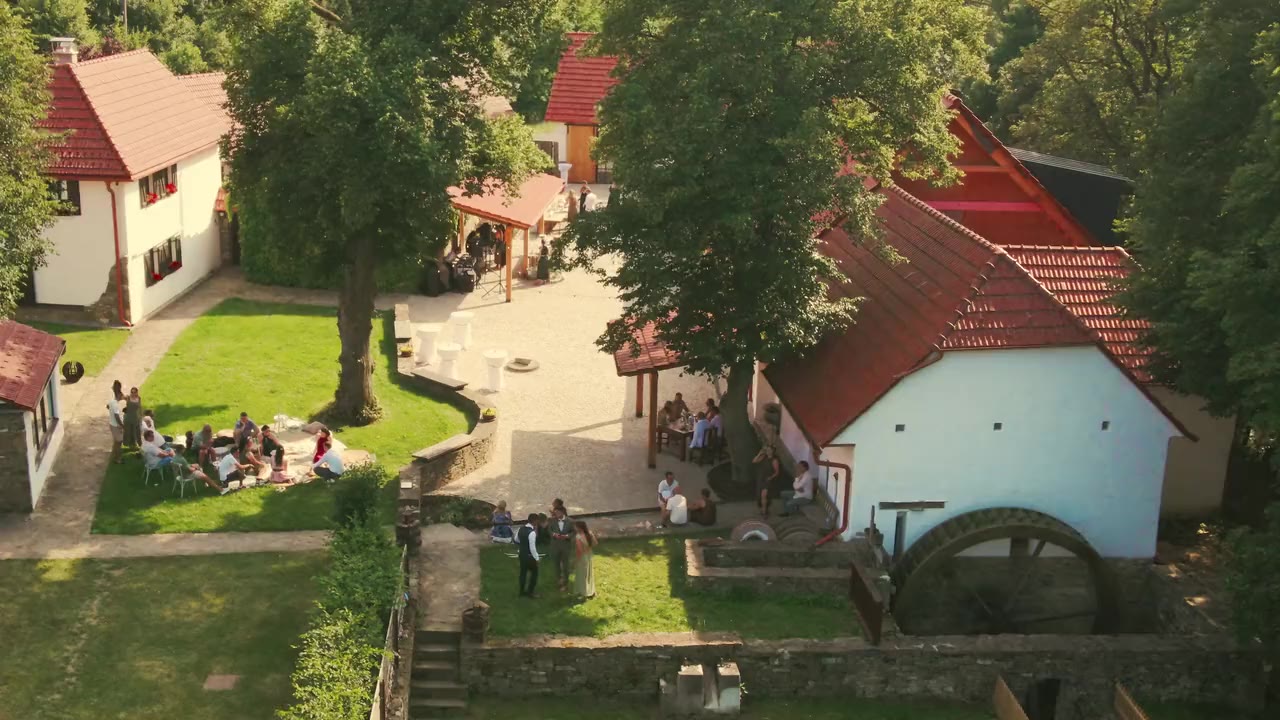 Nádvoří mlýna z výšky, hosté sedí v trávě.